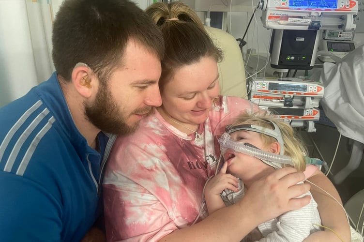 Amelia, Jodie and Rich in hospital. See SWNS story SWLNheart. A mum who took her 17-month-old daughter to the GP for a suspected ear infection  was told  the toddler was 'waiting at God's door' and had to be put on a heart transplant list. Amelia Bolter, now 22-months-old, was taken to her doctor's in Chippenham, Wilts by her mother Jodie Woolford, 31,on June 16 this year. Jodie thought Amelia was suffering from an ear infection or teething issues as she kept rubbing her ear, but was shocked when the doctor found her heart rate racing between at 180-220 beats per minute. She was immediately rushed to Bath Hospital, before being transferred to Bristol Children's hospital the same day.  