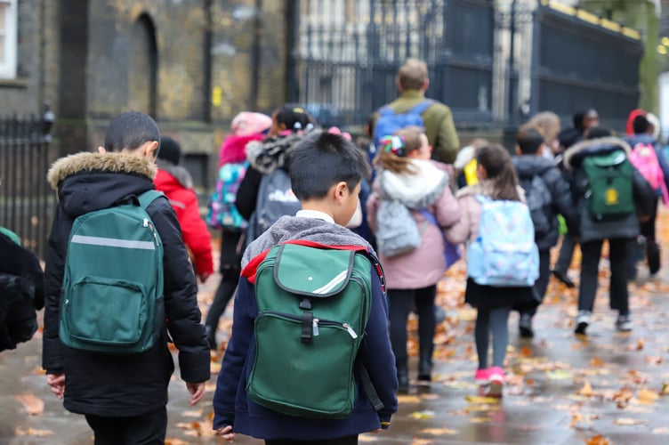 Multi-Cultural Children (asian, Indian, Chinese, Caucasian) primary student or kids and teacher carrying  school bag walk in street in rain winter day, with maple leaves on ground. back view