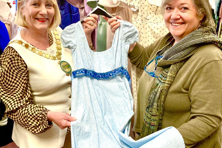  Rusette Auton (right) presents a Regency dress to Cllr Karen Walker, Chair of B&NES Council, standing before a collection of gowns created by Bath Theatrical, specifically for the Jane Austen 250th anniversary celebrations.